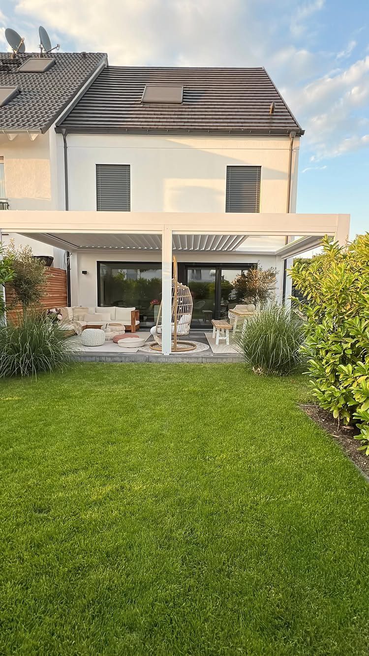 20 Backyard Gardening Inspiration Ideas for Every Outdoor Space 4 A white modern pergola structure covering a furnished patio area next to a green lawn.