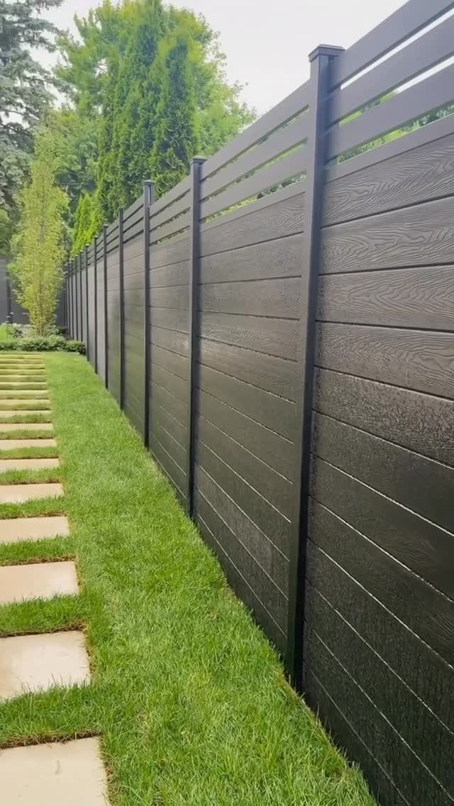 20 Backyard Gardening Inspiration Ideas for Every Outdoor Space 8 A modern black horizontal slat fence bordering a green lawn and stone stepping path.
