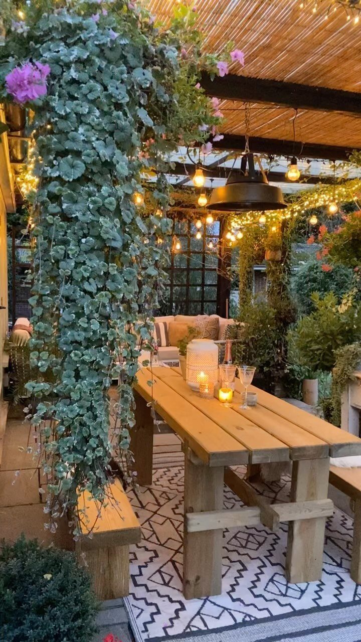20 Backyard Gardening Inspiration Ideas for Every Outdoor Space 17 Wooden outdoor dining table and benches set under a pergola with hanging plants and string lights.