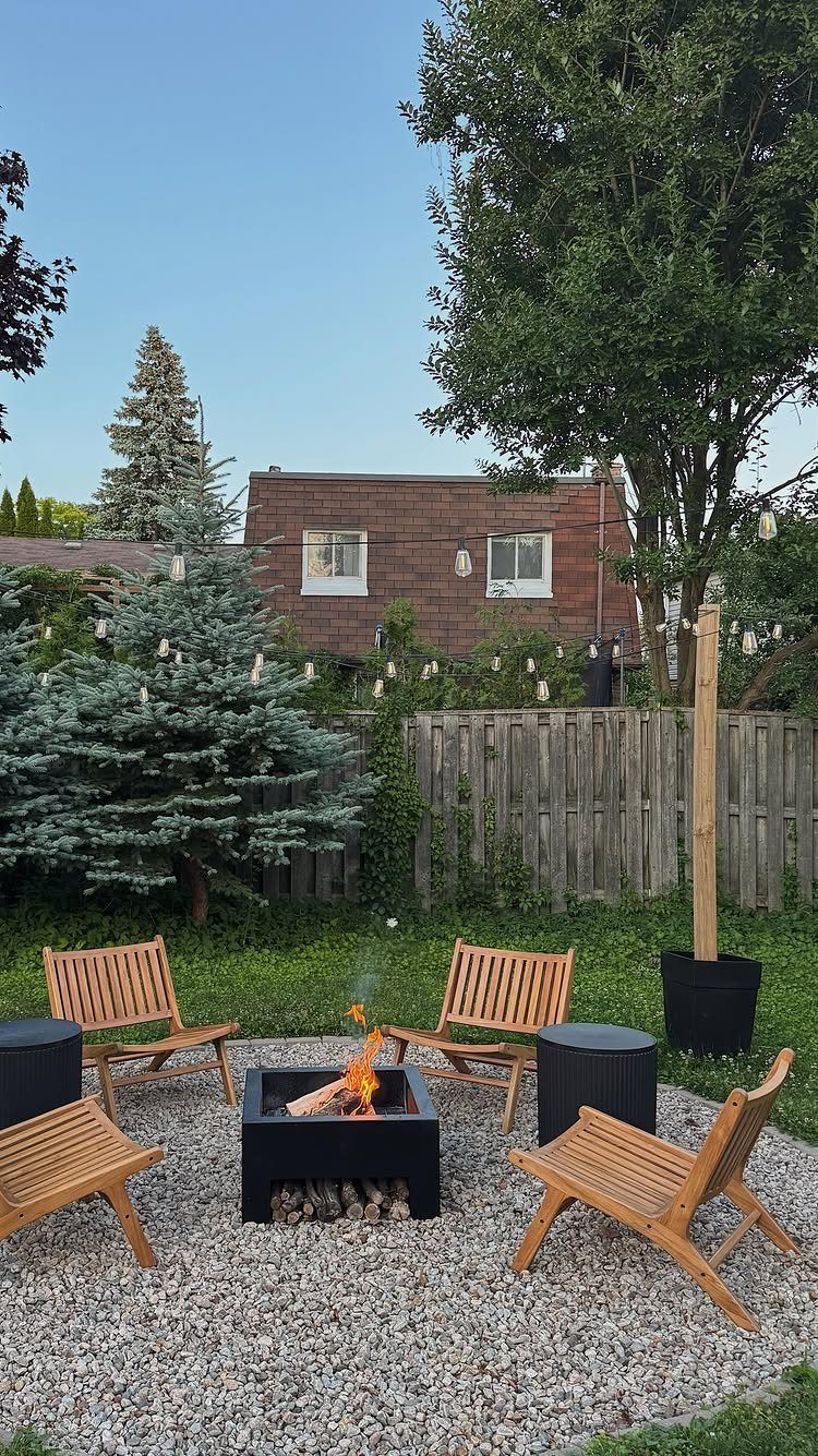 20 Backyard Gardening Inspiration Ideas for Every Outdoor Space 3 A black square fire pit with a burning fire surrounded by wooden chairs on gravel.