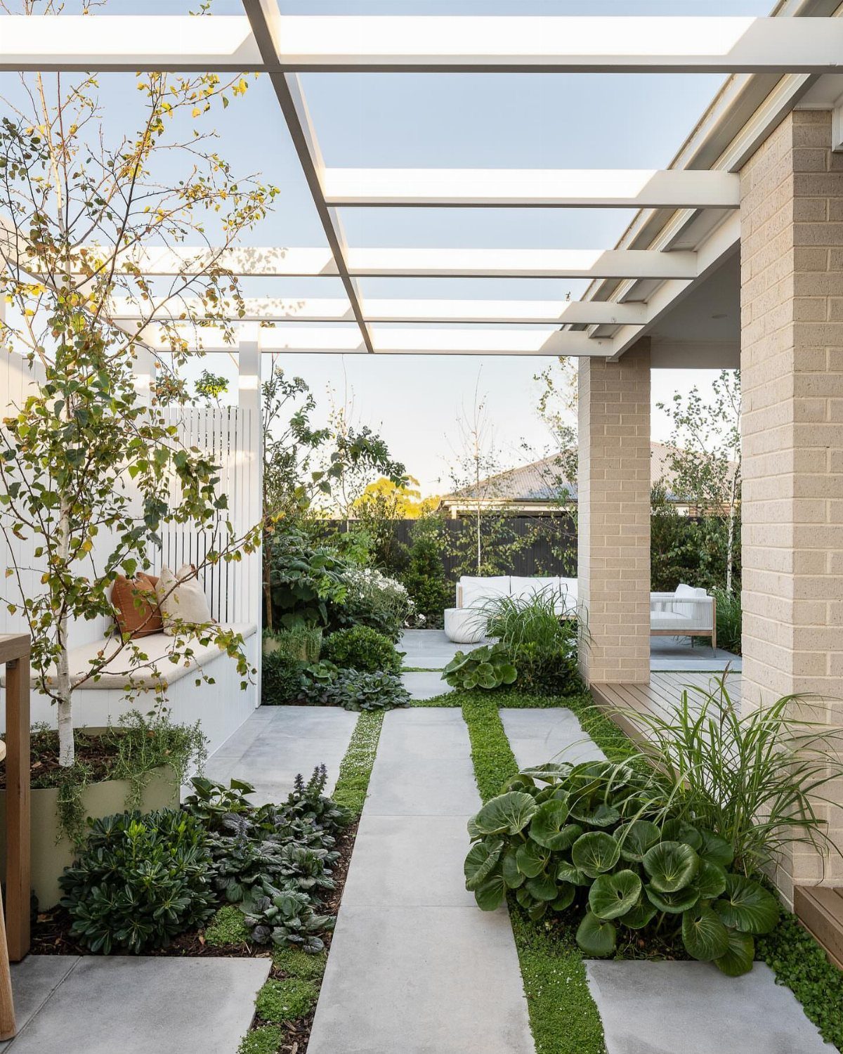 20 Backyard Gardening Inspiration Ideas for Every Outdoor Space 1 Concrete pavers with grass strips lead through a lush garden toward a white outdoor patio seating area.