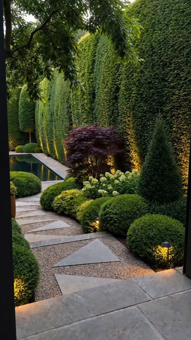 21 Backyard Landscape Design Ideas for Outdoor Living 8 Tall green privacy hedges and manicured shrubs line a stone pathway in a landscaped backyard.
