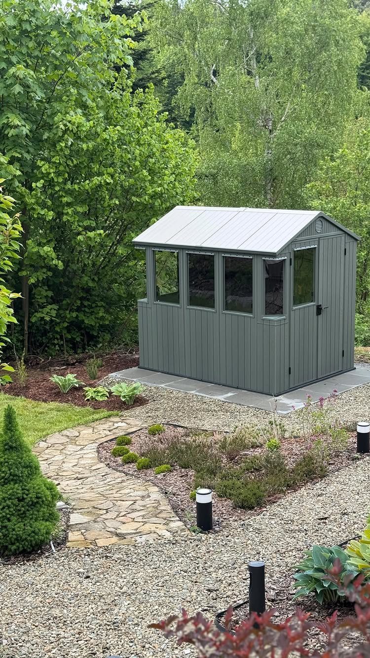 21 Backyard Landscape Design Ideas for Outdoor Living 19 A grey metal tool shed with windows situated in a landscaped garden with stone paths.