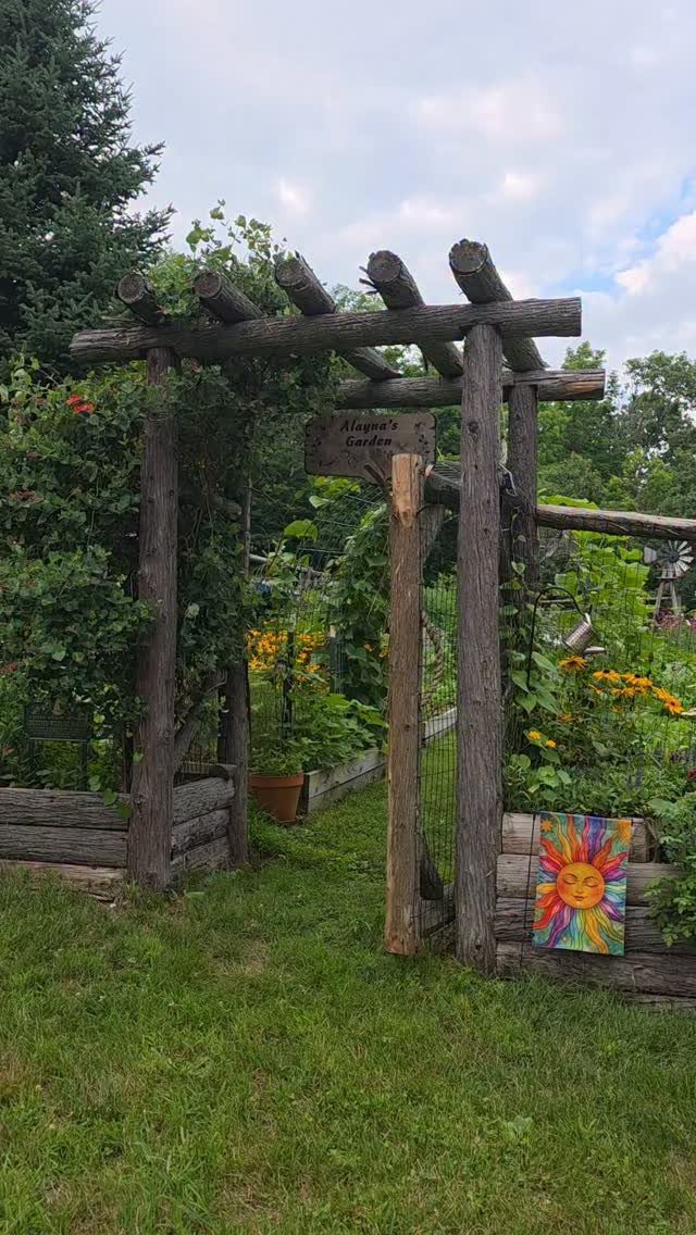9 Backyard Vegetable Gardens for Any Space 6 A rustic wooden pergola entrance leading into a lush backyard vegetable garden with blooming flowers.