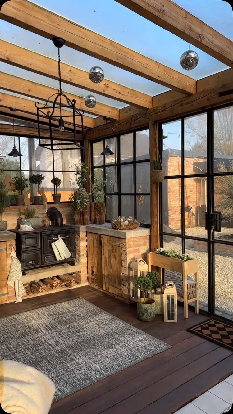 A rustic kitchen setup inside a glass-roofed greenhouse with wooden beams and many potted plants.