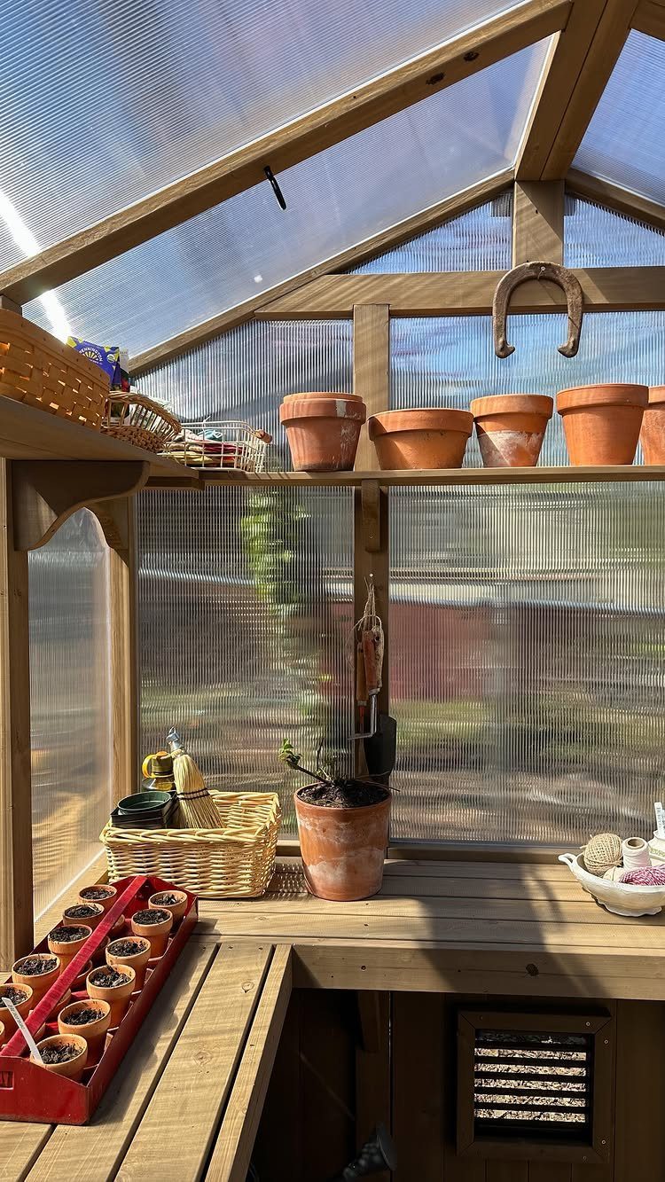 Wooden greenhouse interior with terracotta pots and seedling trays on a workbench.