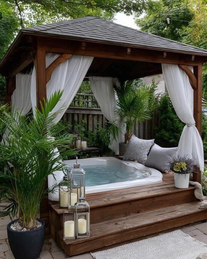 7 Covered Hot Tub Ideas for Backyard Privacy and Style (2026) 6 A wooden gazebo with white curtains enclosing a hot tub on a raised deck.