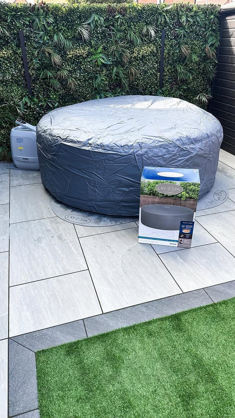 7 Covered Hot Tub Ideas for Backyard Privacy and Style (2026) 4 A grey circular hot tub cover on a tiled patio next to its product box.