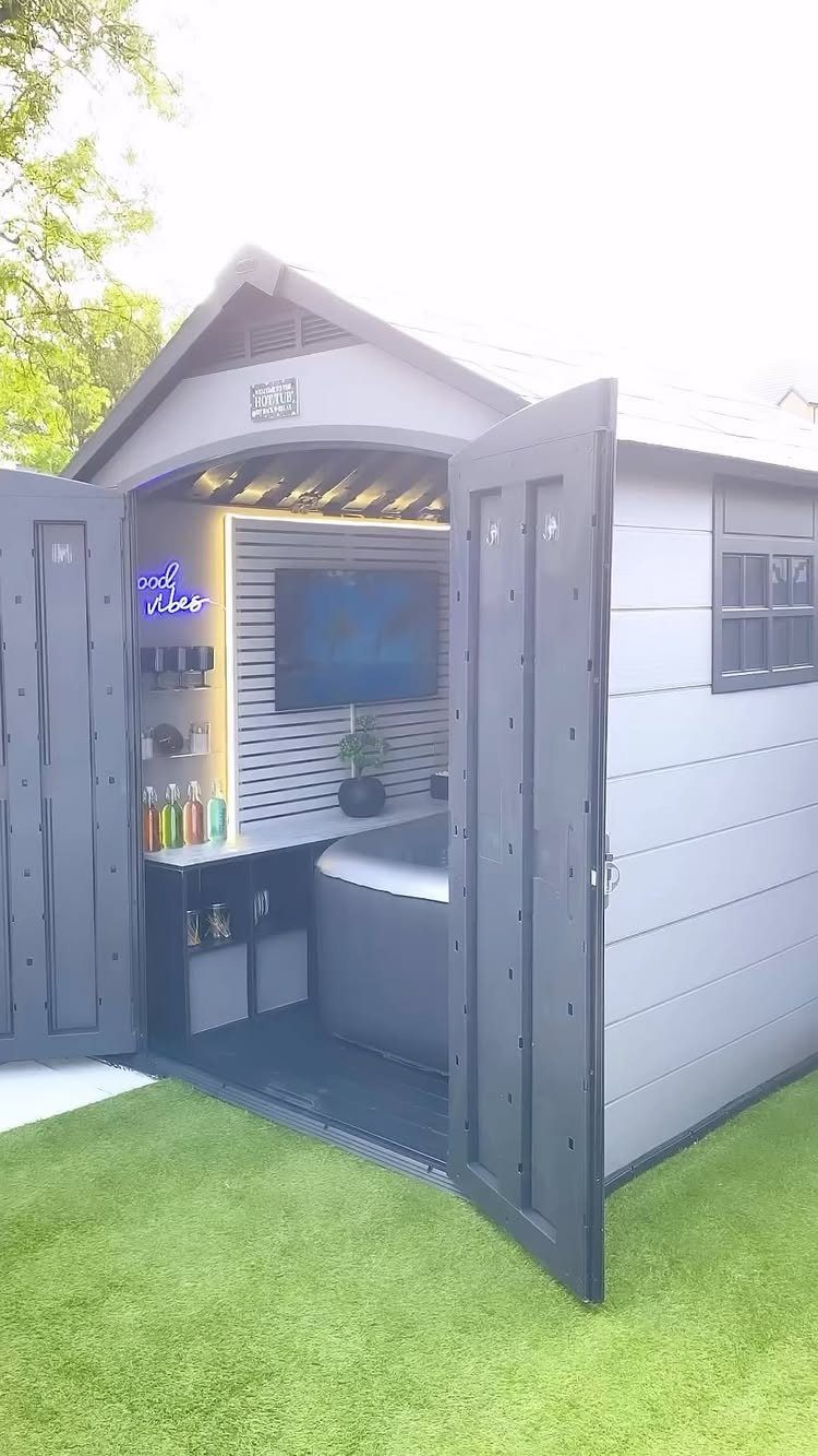 7 Covered Hot Tub Ideas for Backyard Privacy and Style (2026) 7 A grey garden shed with open doors revealing a hot tub and television inside.