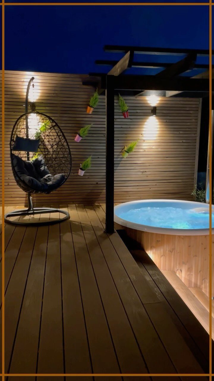 7 Covered Hot Tub Ideas for Backyard Privacy and Style (2026) 2 A lit hot tub on a wooden deck under a black pergola at night.