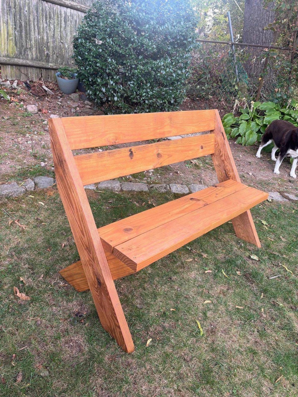 DIY Garden Bench: 8 Plans from Classic Backrests to Cinder Block Builds 4 A wooden garden bench with a backrest sits on a green grass lawn outdoors.