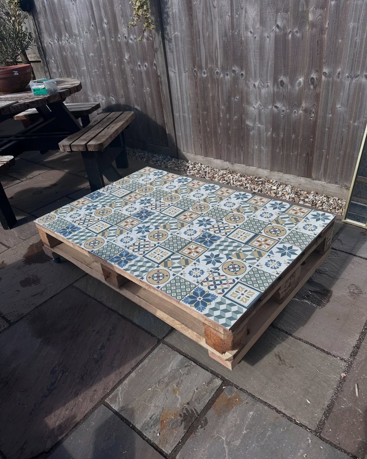 9 DIY Outdoor Furniture Ideas: Pallet Tables to Adirondack Chairs 9 A DIY coffee table made from a wooden pallet topped with patterned blue and white tiles.