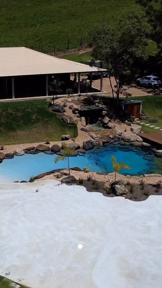 12 Dream Backyard Garden Ideas with Outdoor Kitchens to Natural Pools 12 A natural swimming pool with blue water surrounded by rocks and lush greenery in a backyard.