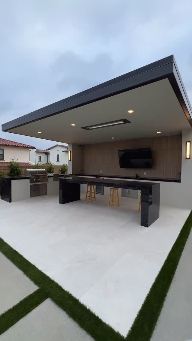 12 Dream Backyard Garden Ideas with Outdoor Kitchens to Natural Pools 1 Modern outdoor kitchen with black countertops, built-in grill, and a television under a covered patio.