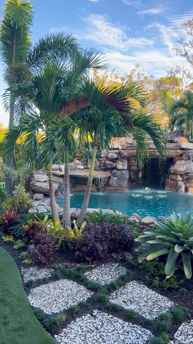 12 Dream Backyard Garden Ideas with Outdoor Kitchens to Natural Pools 7 Tropical backyard with a swimming pool, rock waterfall, palm trees, and a stone paver path.