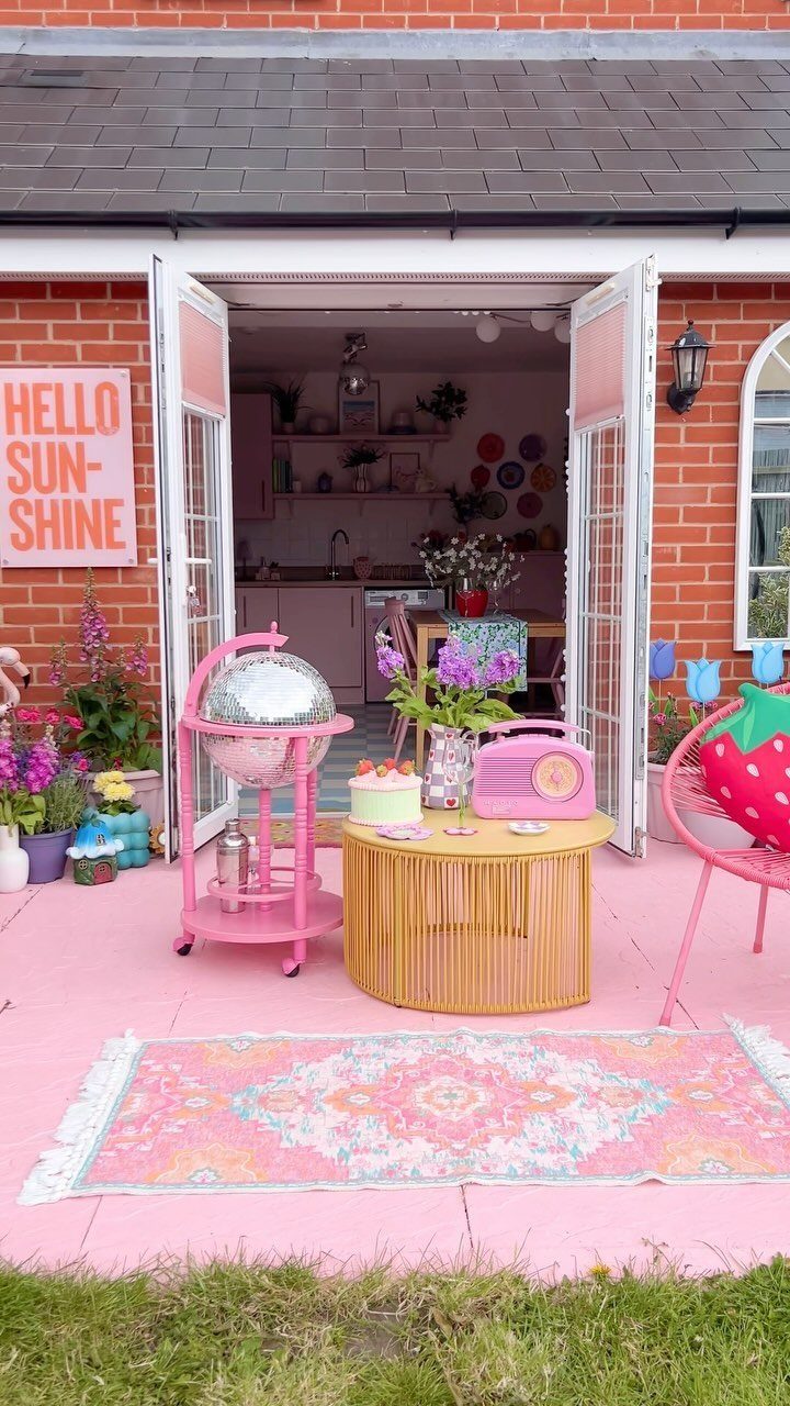 7 Easy DIY Patio Ideas With Paver Floors, Pallets and Gravel 2 Pink painted concrete patio with colorful outdoor furniture and a patterned rug in a garden setting.