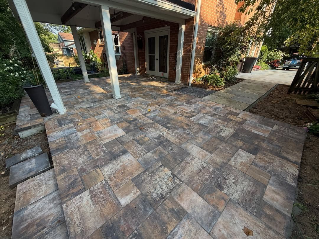 7 Easy DIY Patio Ideas With Paver Floors, Pallets and Gravel 1 Stone pavers in various earth tones forming a new patio under a white porch structure.