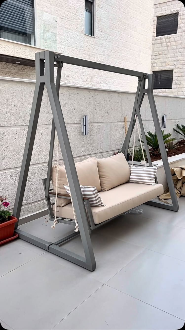 7 Easy DIY Patio Ideas With Paver Floors, Pallets and Gravel 7 A grey metal outdoor swing seat with beige cushions on a tiled patio.