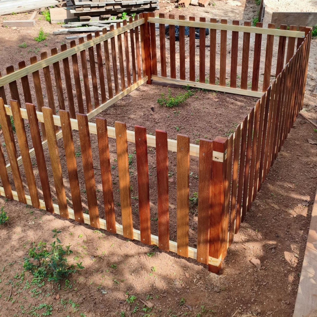 7 Garden Bed Fence Ideas to Protect Your Plants 6 A small wooden picket fence enclosing a rectangular patch of dirt in a garden.