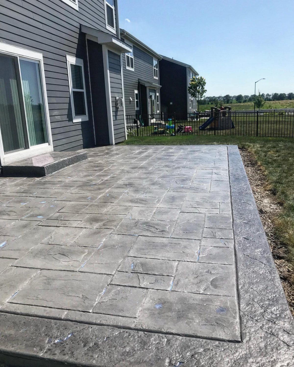 A grey stamped concrete patio with a stone pattern next to a house.