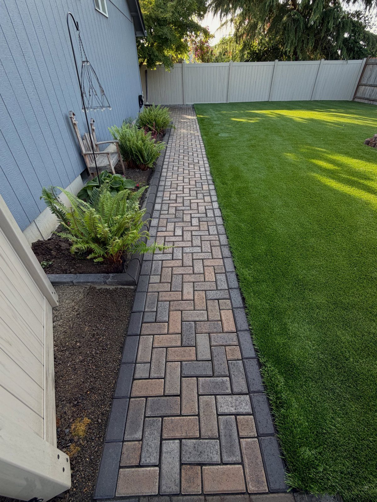 16 Lawn Border Ideas from Steel to Glass Bottle Edges 4 A herringbone pattern paving stone walkway borders a green lawn next to a blue house.