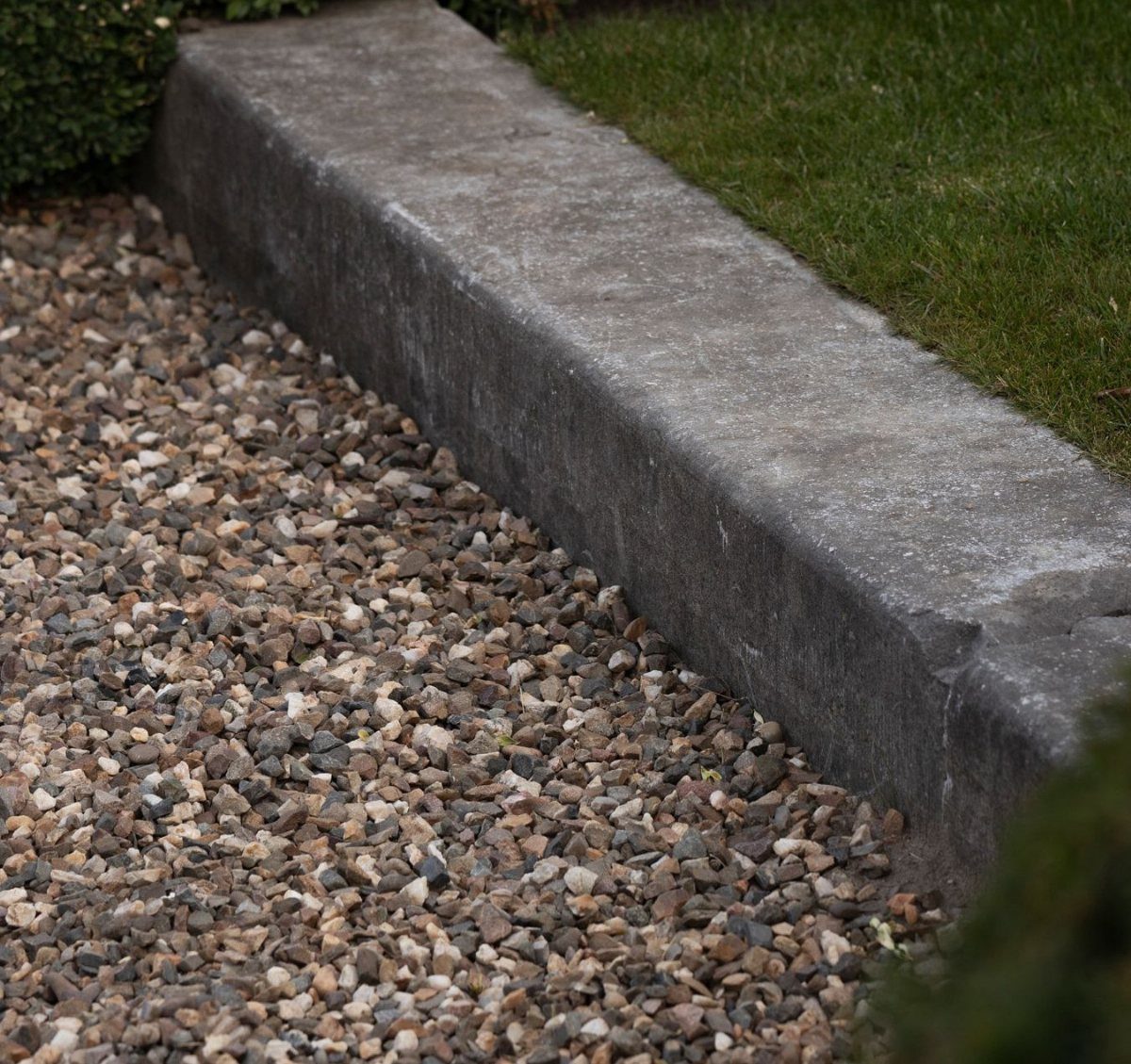 16 Lawn Border Ideas from Steel to Glass Bottle Edges 14 A grey concrete edging strip bordering a green lawn and a gravel path.