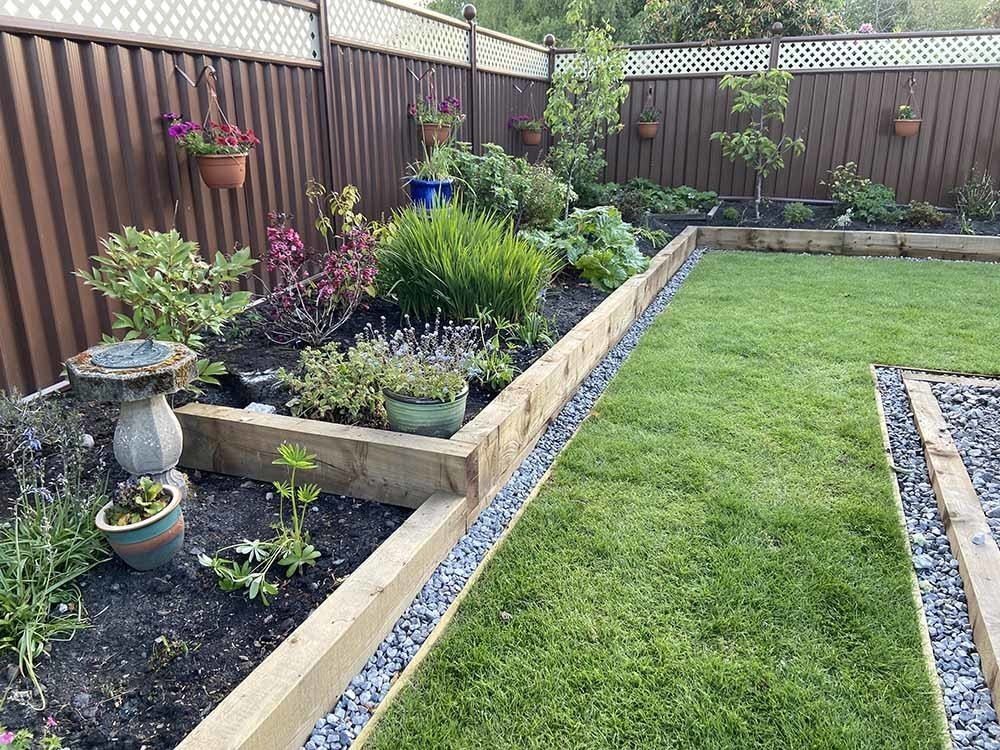 16 Lawn Border Ideas from Steel to Glass Bottle Edges 10 Wooden railway sleepers forming raised garden beds around a lush green lawn in a backyard.