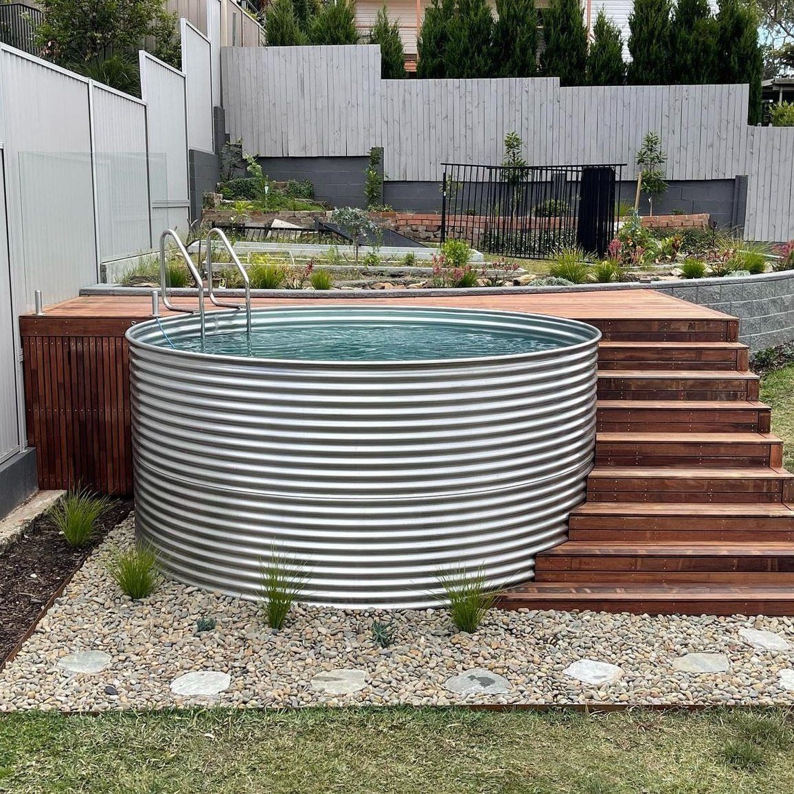 A circular corrugated metal plunge pool integrated into a wooden deck with stairs and surrounding gravel.