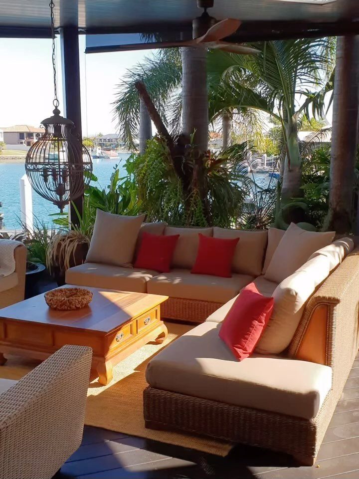 Wicker outdoor sectional sofa with tan cushions and red pillows on a sunny patio.