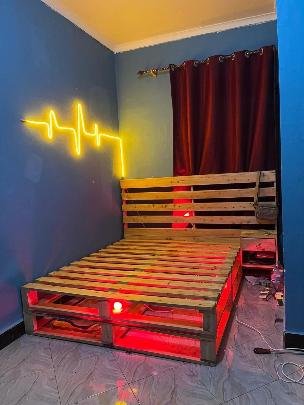 A wooden pallet bed frame with red under-lighting against a blue wall.