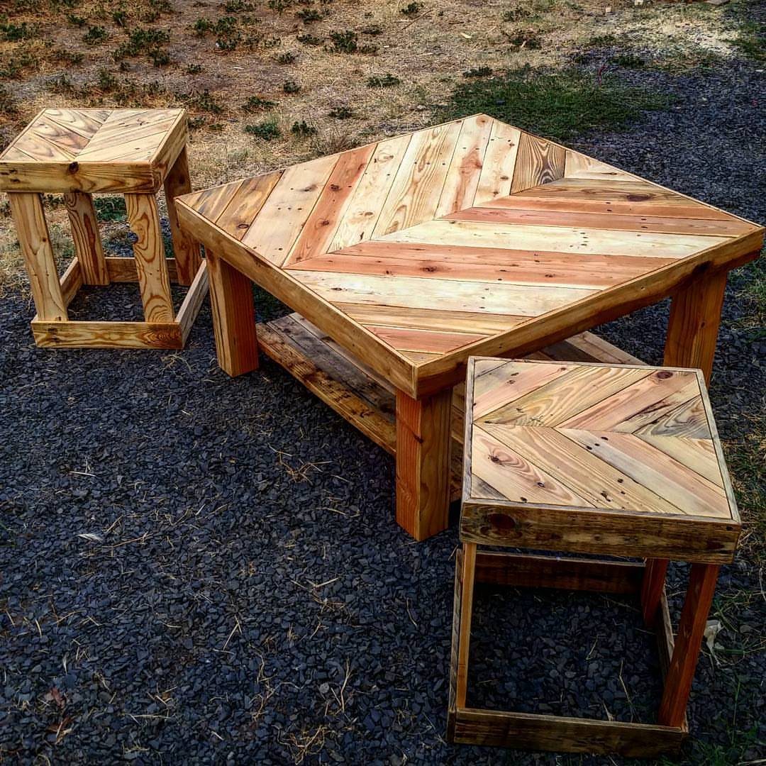 A wooden chevron pattern coffee table with two matching small wooden stools on gravel.