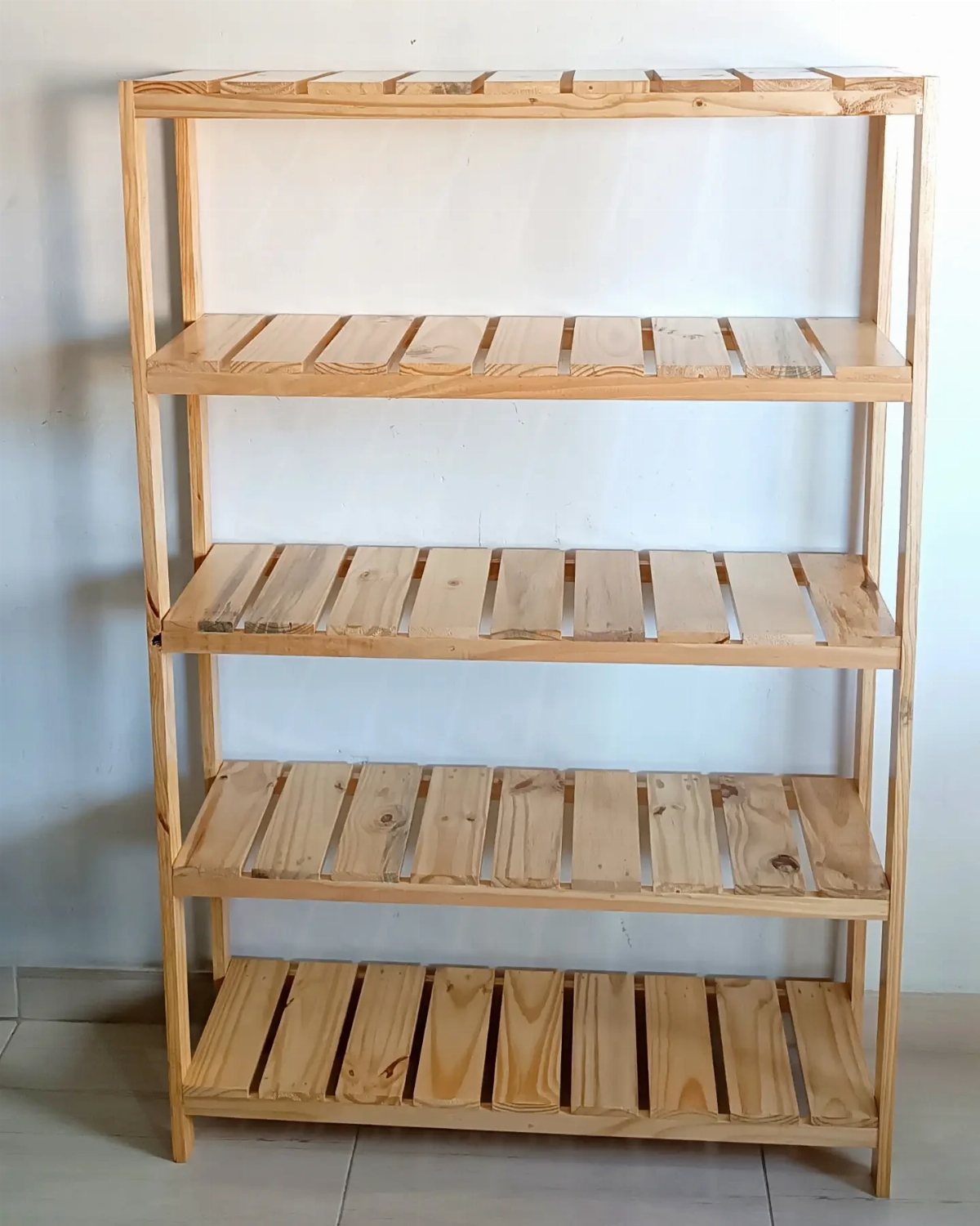 A four-tier wooden shelving unit constructed from light-colored pallet slats against a white wall.