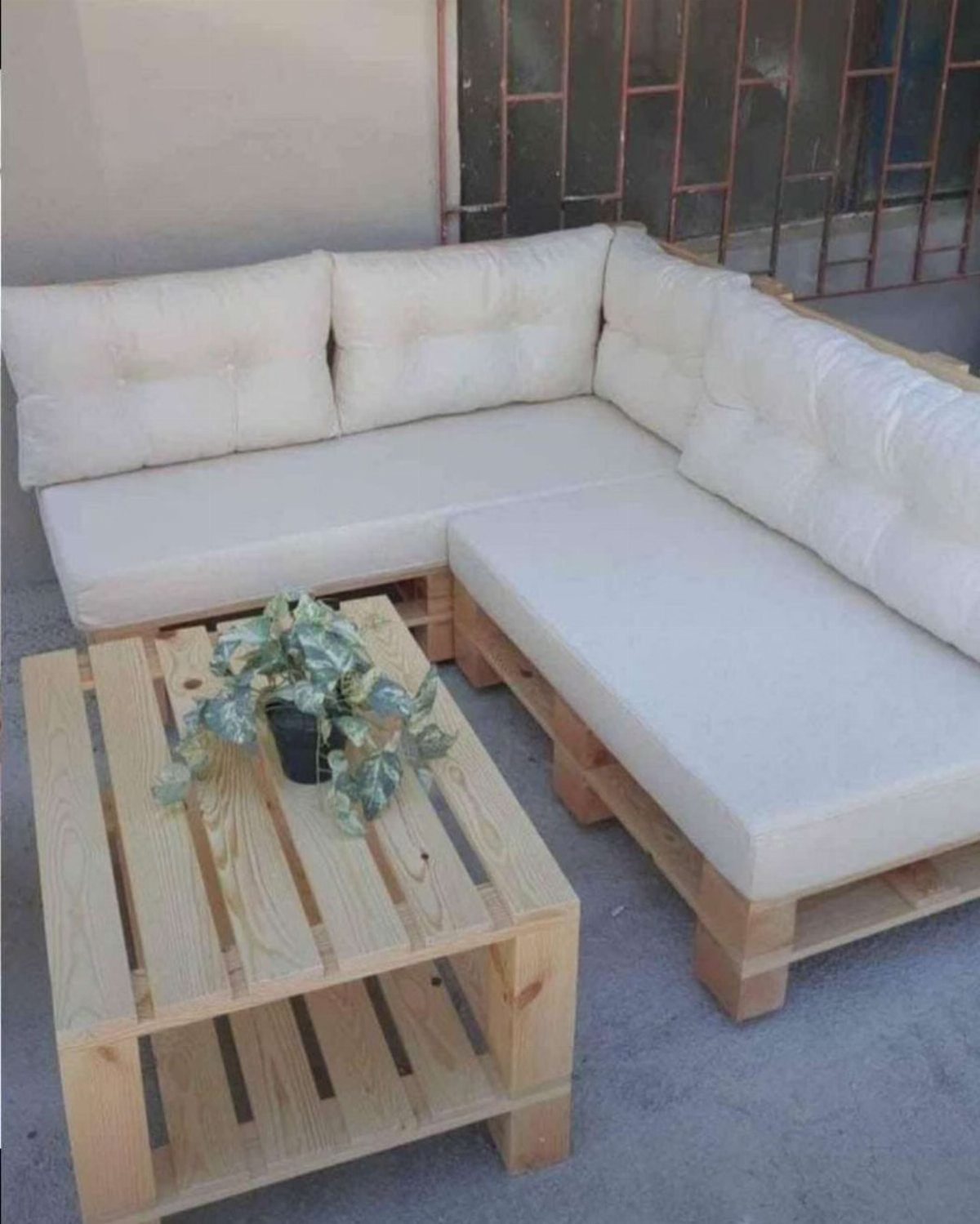 L-shaped pallet sofa with white cushions and a matching pallet coffee table on a patio.