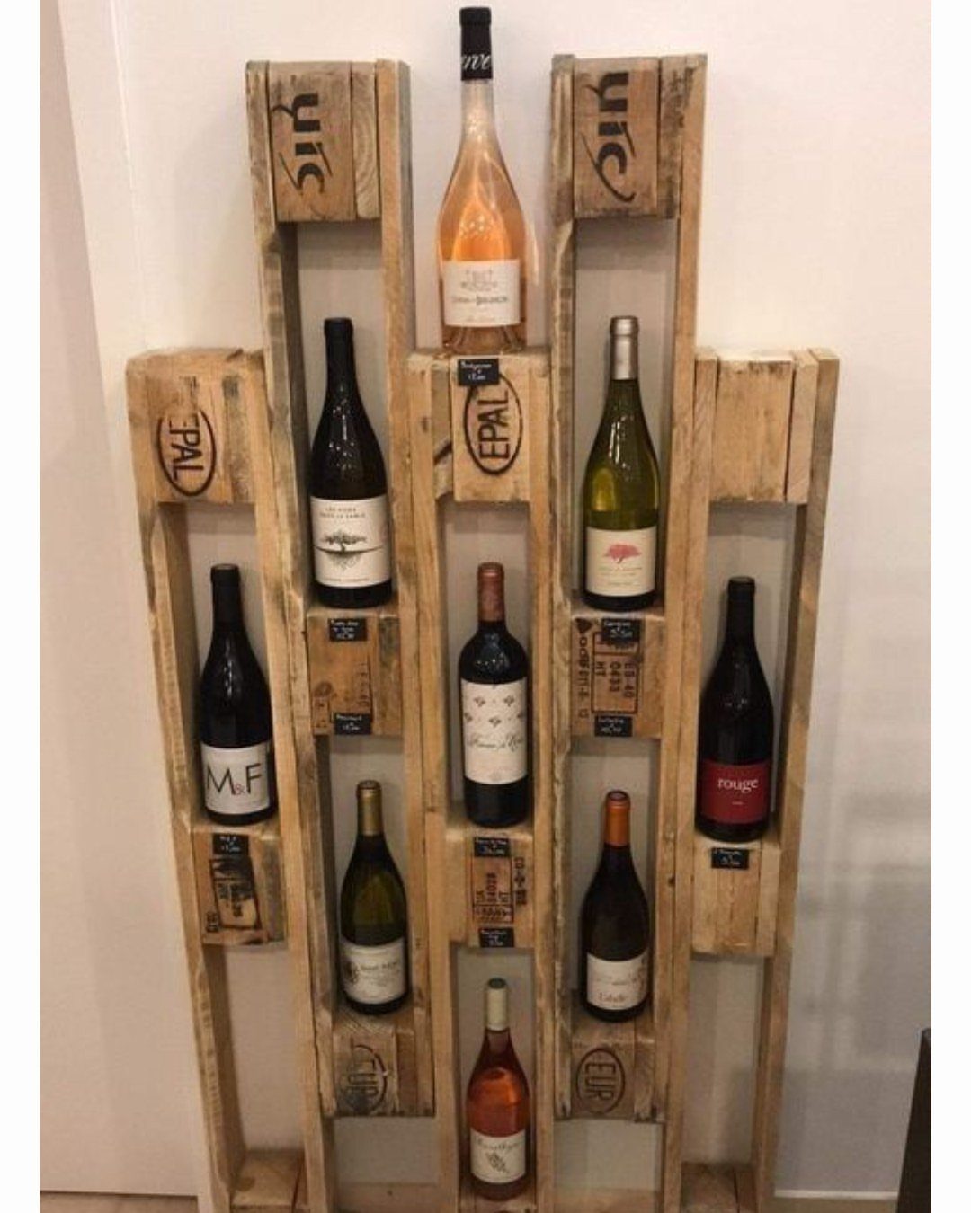 A wooden pallet wine rack mounted on a white wall holding several wine bottles.