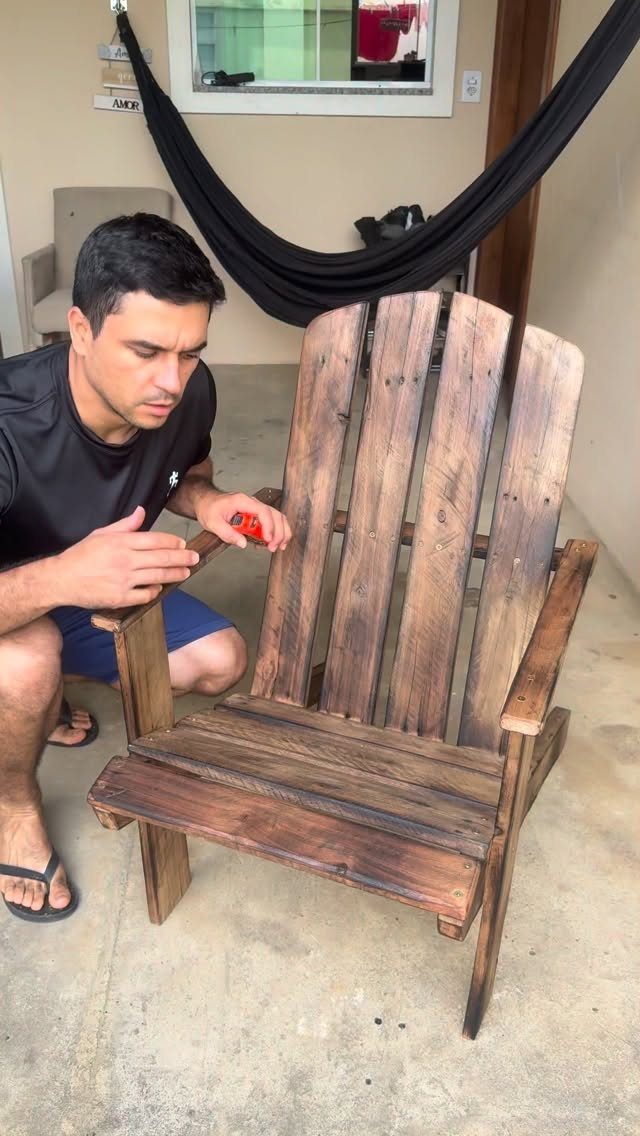 A man works on a rustic wooden chair constructed from dark stained pallet wood slats.