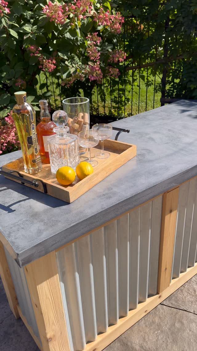 A DIY outdoor bar with a concrete top and corrugated metal panels holding drinks.