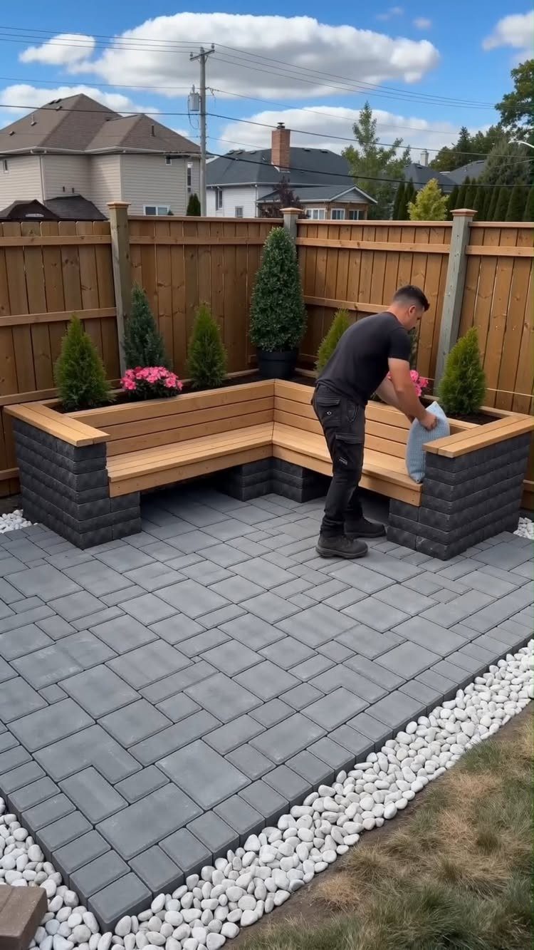 A man building a wooden corner bench on a grey stone paver patio.