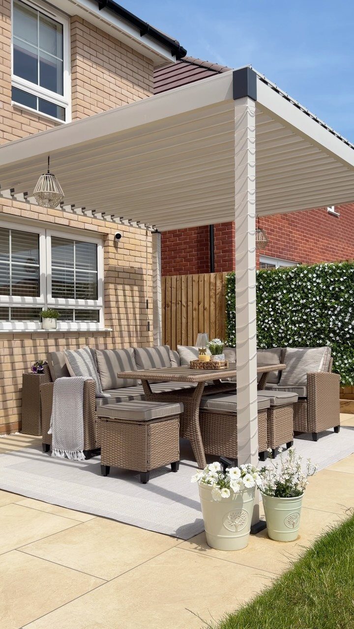 Wicker patio dining set with striped cushions on a grey outdoor rug under a pergola.