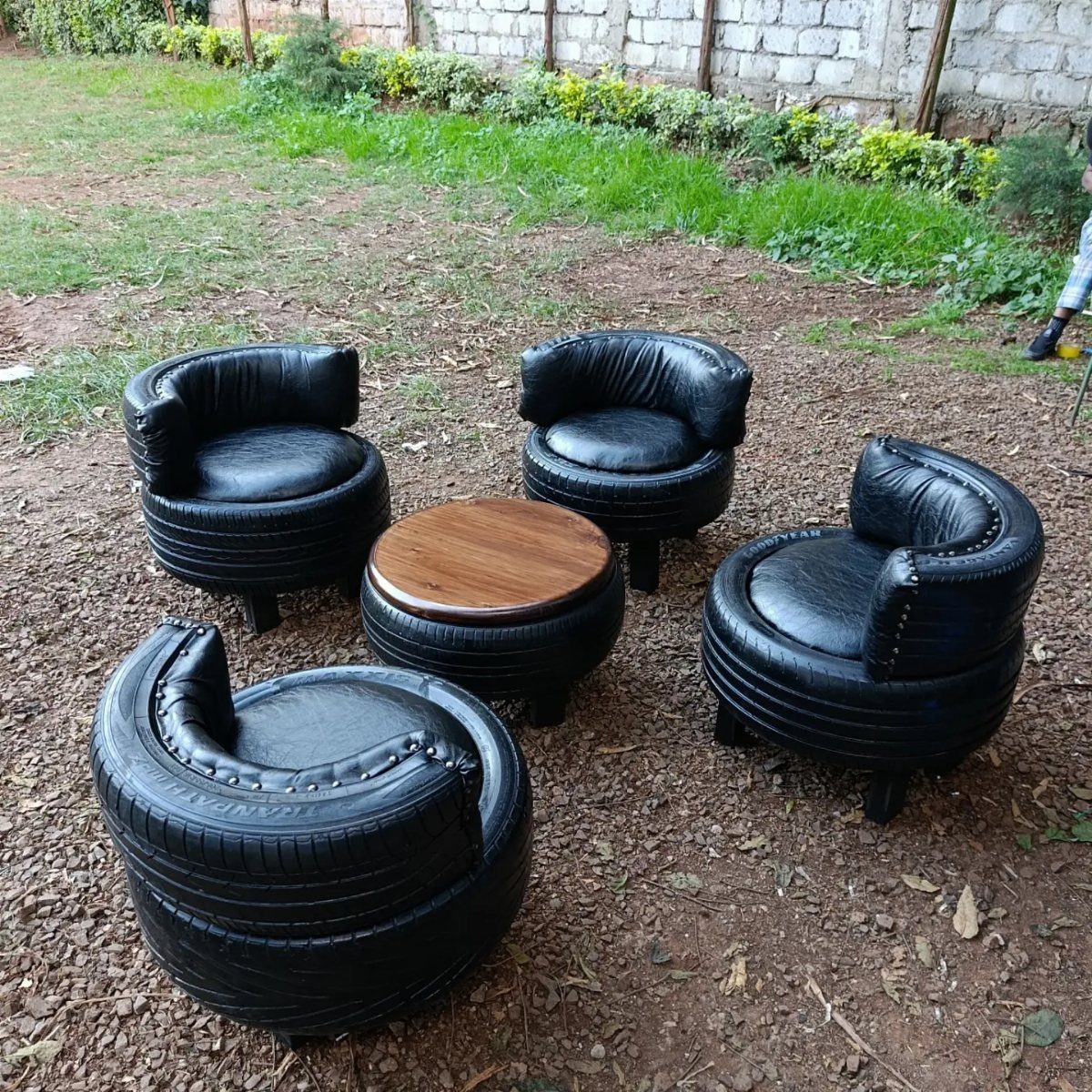 Four black leather upholstered chairs and a coffee table made from recycled tires on dirt.