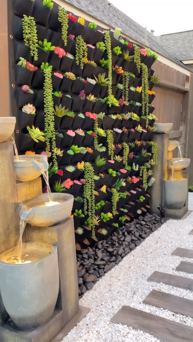 A black vertical garden wall featuring various colorful succulents and green plants against a wooden fence.