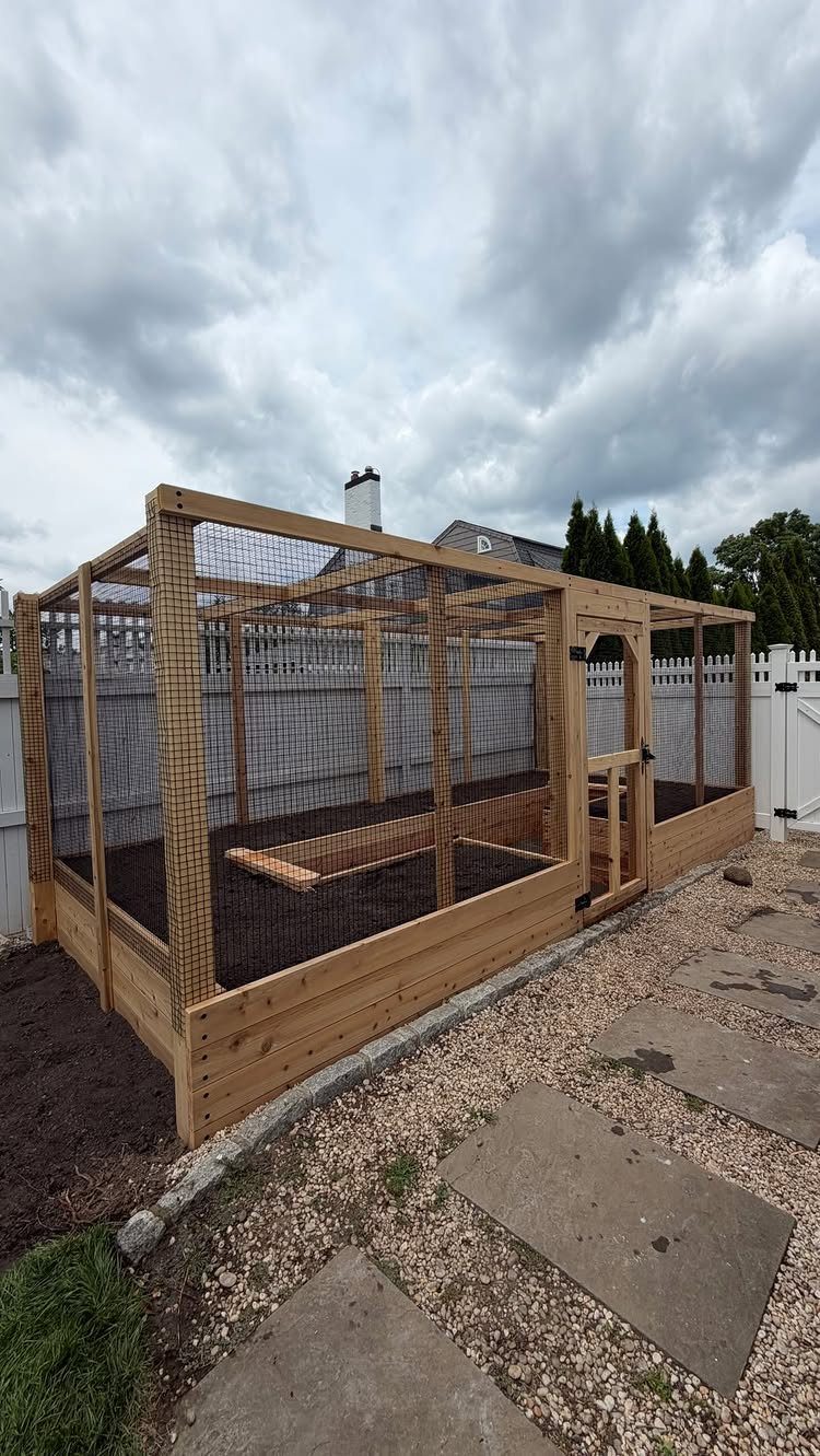 8 Raised Garden Bed Fence Ideas for Plants, Privacy, and Pests 5 A large wooden garden enclosure with wire mesh walls and a small access door.