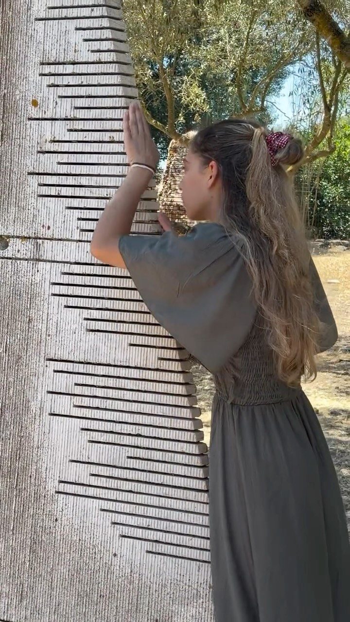 A woman touches the textured grooves of a large wooden outdoor sculpture.