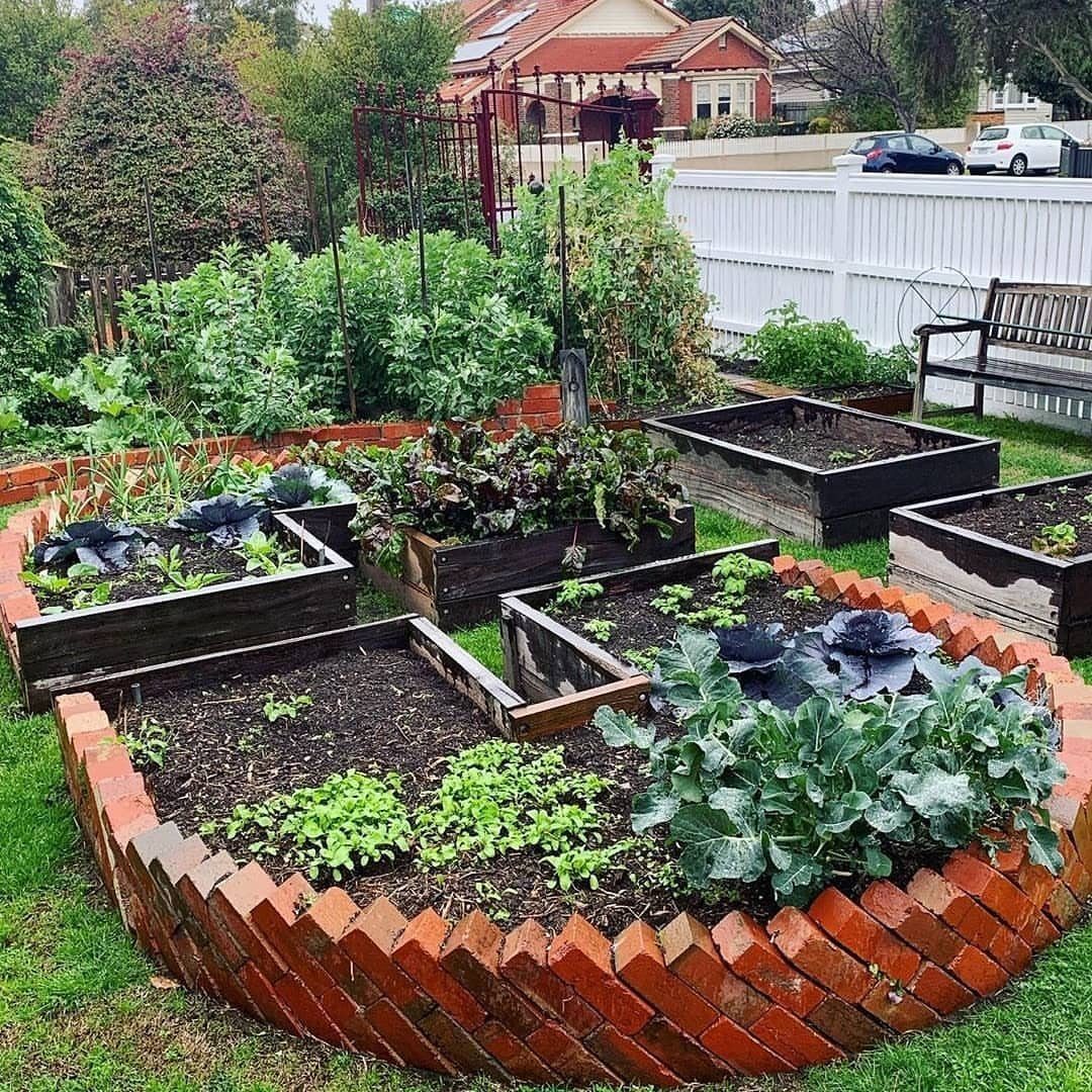 Circular brick garden bed containing several wooden planter boxes filled with various green leafy vegetables.