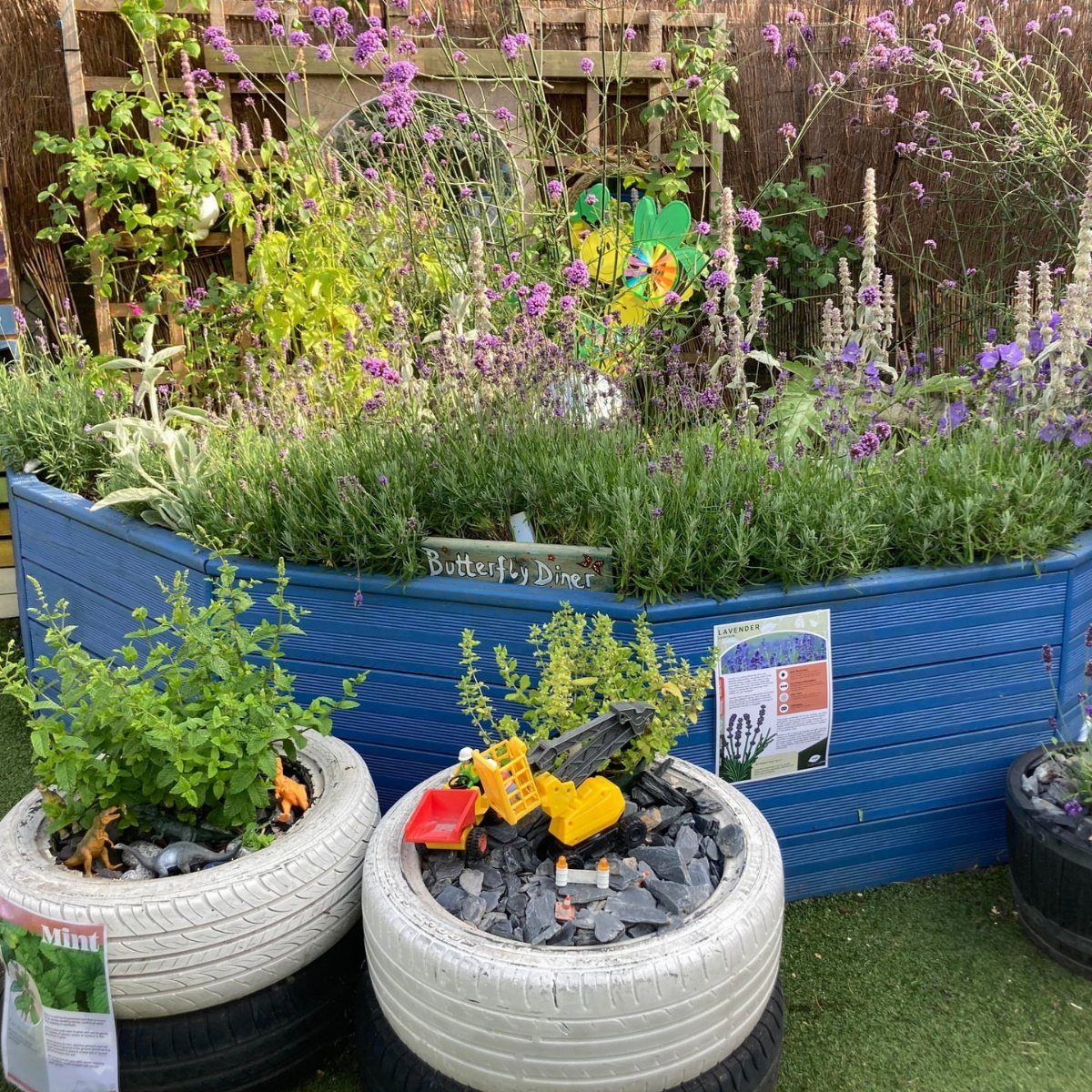 A blue wooden garden bed with purple flowers and a sign reading Butterfly Diner.