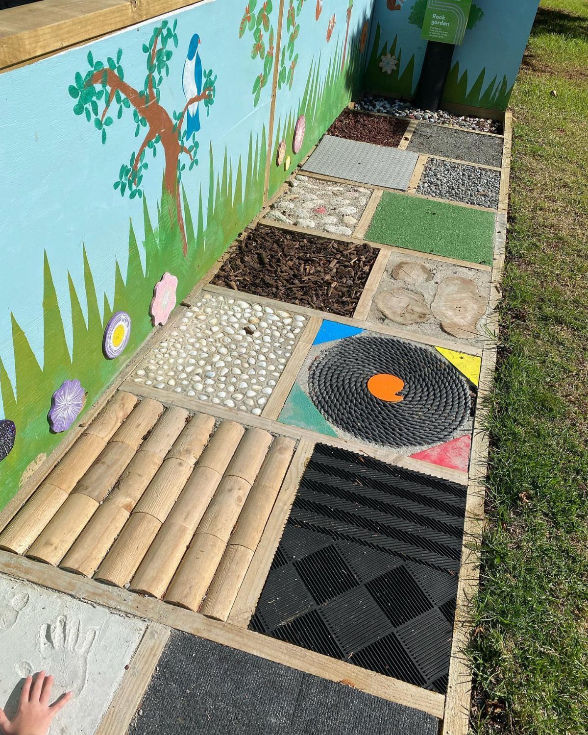 A sensory path featuring diverse textures like wood, pebbles, and rubber mats alongside a painted wall.