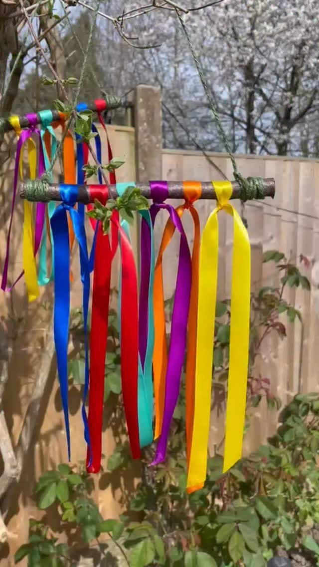 Brightly colored satin ribbons hanging from a wooden stick in a garden setting.
