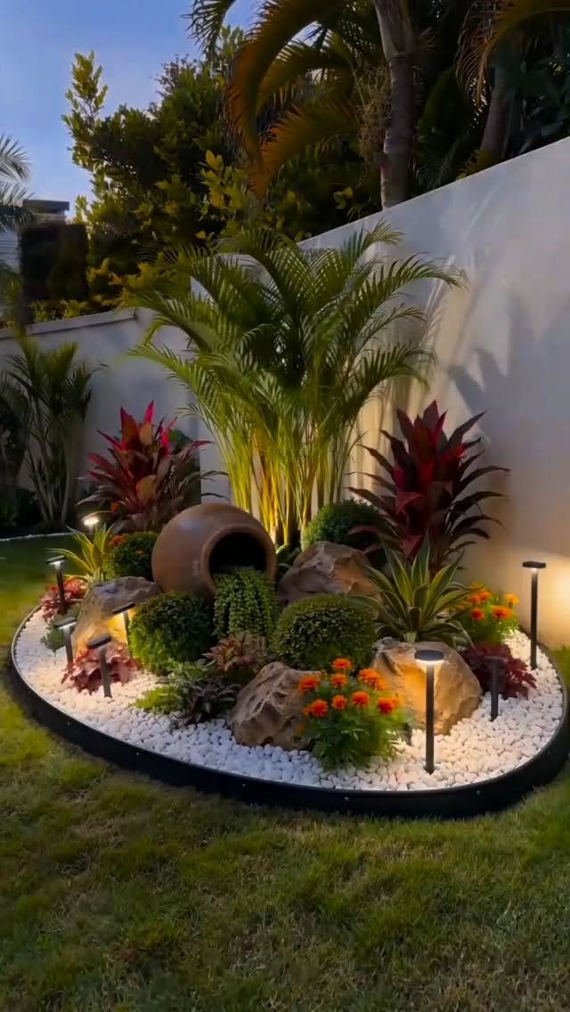 A landscaped garden bed featuring various textured plants, rocks, and solar lights against a white wall.