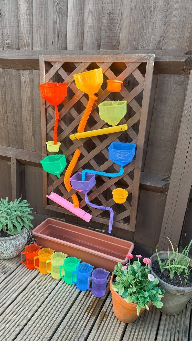 Colorful plastic tubes and funnels attached to a wooden trellis in an outdoor garden setting.