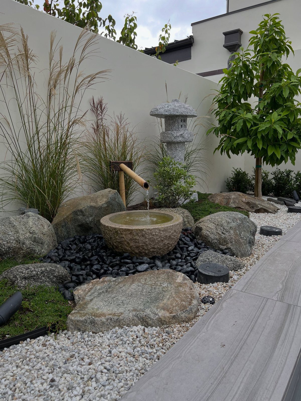 A stone water basin with a bamboo spout surrounded by rocks and gravel in a Zen garden.