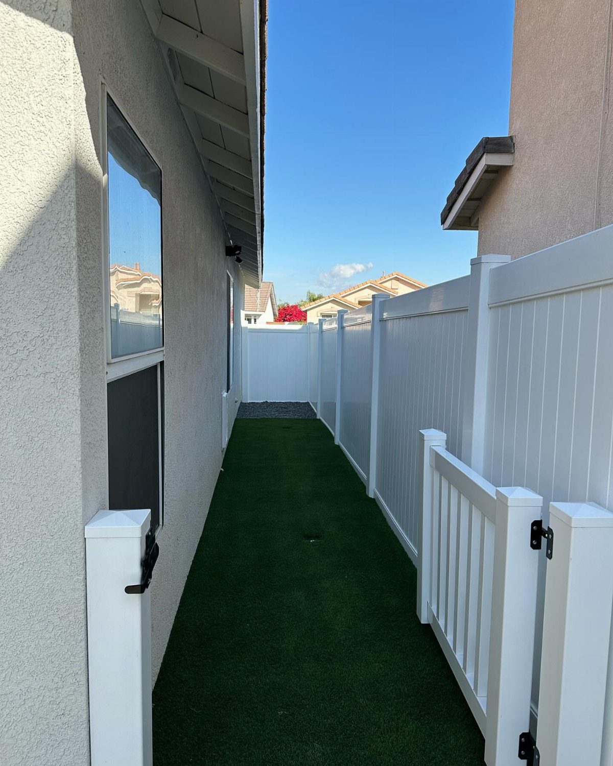 Artificial turf strip running alongside a white vinyl fence and a house wall.